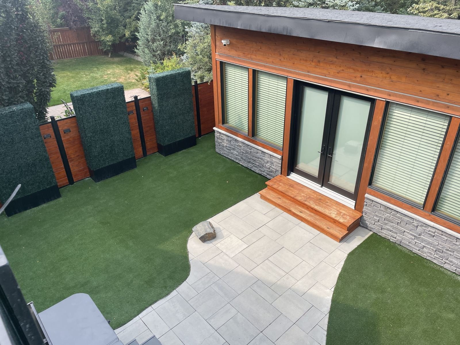 Artificial turf yard with hedge fencing and stone patio